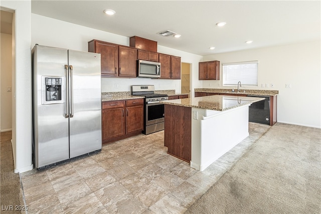 kitchen with light carpet, stainless steel appliances, a center island, light stone counters, and sink