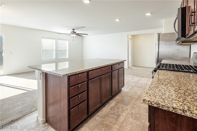 kitchen featuring light stone counters, stainless steel appliances, light carpet, and a center island