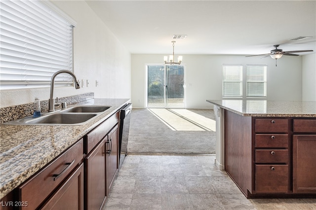 kitchen with light stone counters, stainless steel dishwasher, pendant lighting, ceiling fan with notable chandelier, and sink