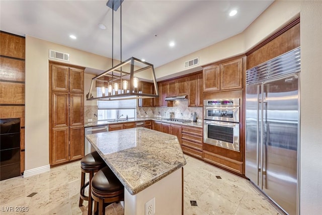 kitchen featuring decorative light fixtures, a center island, light stone counters, a kitchen bar, and appliances with stainless steel finishes