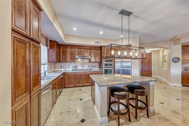 kitchen featuring appliances with stainless steel finishes, pendant lighting, light stone counters, a kitchen island, and tasteful backsplash