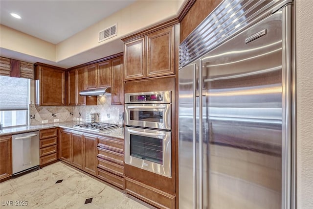 kitchen with light stone countertops, appliances with stainless steel finishes, and backsplash