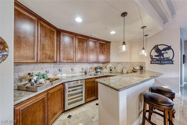 kitchen with a breakfast bar area, wine cooler, kitchen peninsula, light stone counters, and sink