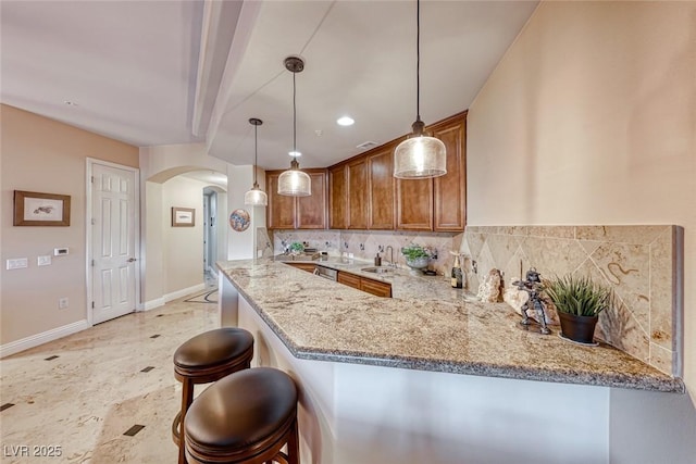 kitchen with light stone counters, kitchen peninsula, hanging light fixtures, a breakfast bar, and backsplash