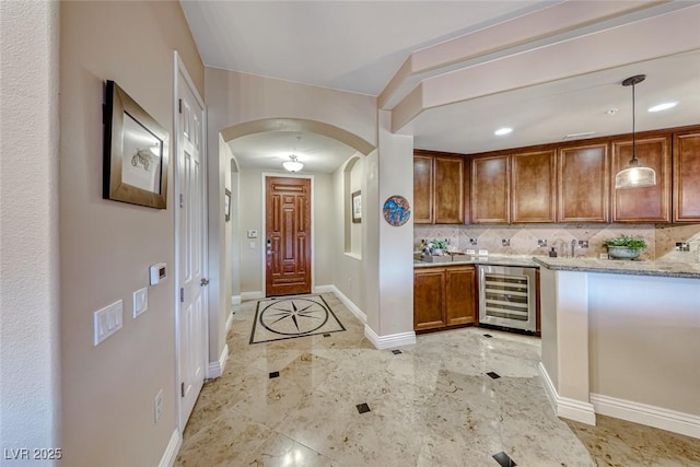 kitchen with beverage cooler, tasteful backsplash, pendant lighting, and light stone counters