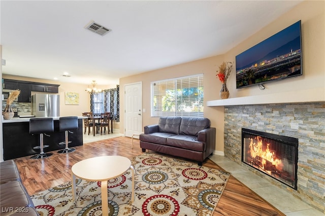 living room featuring light wood-style flooring, visible vents, a notable chandelier, and a stone fireplace