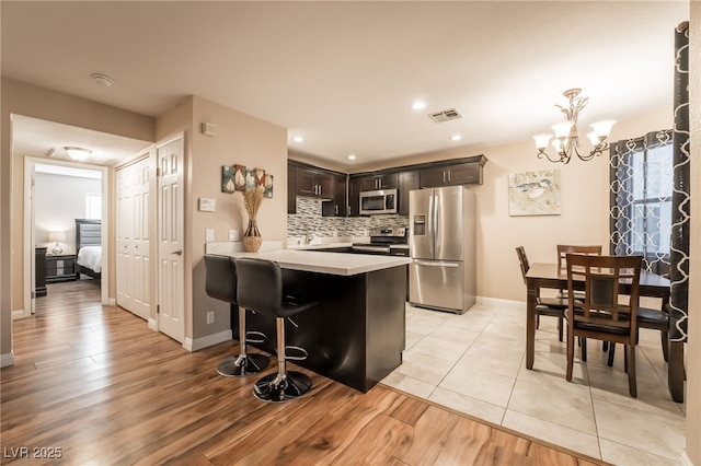 kitchen with stainless steel appliances, backsplash, a chandelier, and light hardwood / wood-style floors