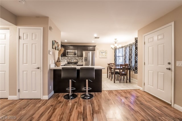 kitchen with a breakfast bar area, stainless steel appliances, kitchen peninsula, a notable chandelier, and tasteful backsplash