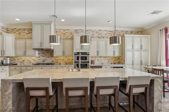 kitchen featuring a large island with sink, decorative light fixtures, ornamental molding, and light stone counters