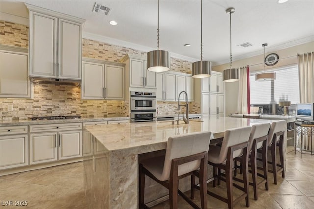 kitchen featuring decorative light fixtures, crown molding, light stone counters, and an island with sink