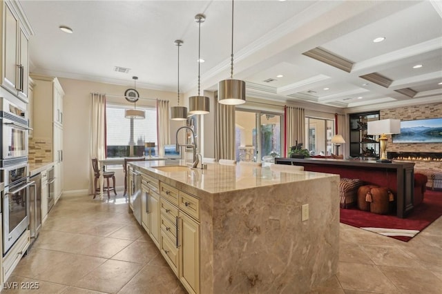 kitchen with light stone countertops, beam ceiling, cream cabinetry, coffered ceiling, and sink