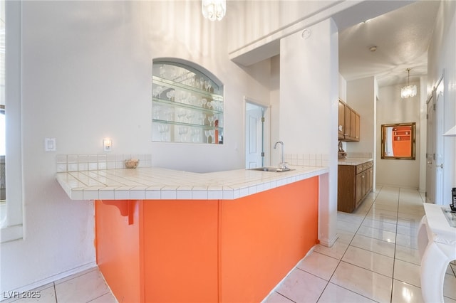 kitchen featuring sink, washer / clothes dryer, tile countertops, light tile patterned floors, and kitchen peninsula