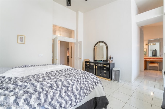 bedroom featuring ceiling fan, connected bathroom, a towering ceiling, and light tile patterned floors