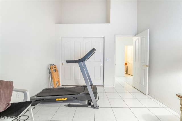 workout room featuring a towering ceiling and light tile patterned floors