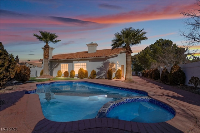 pool at dusk with an in ground hot tub