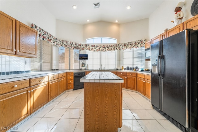 kitchen with tile countertops, a kitchen island, light tile patterned flooring, and black appliances