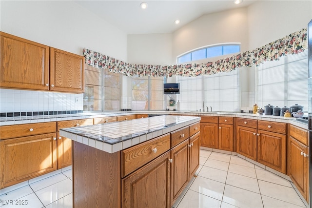 kitchen featuring a center island, light tile patterned floors, tile countertops, a high ceiling, and tasteful backsplash