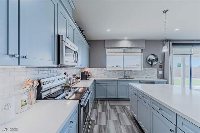 kitchen with sink, hardwood / wood-style floors, decorative backsplash, hanging light fixtures, and appliances with stainless steel finishes