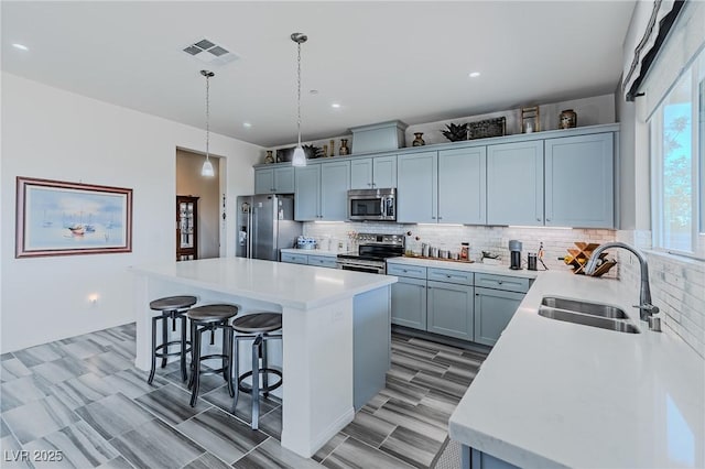 kitchen with pendant lighting, stainless steel appliances, a kitchen island, a breakfast bar area, and sink