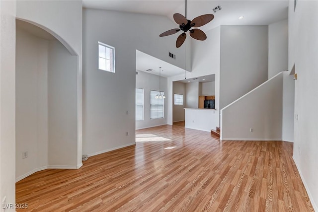 unfurnished living room featuring ceiling fan with notable chandelier, high vaulted ceiling, and light hardwood / wood-style floors