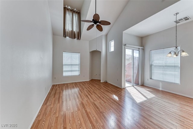 unfurnished living room featuring ceiling fan with notable chandelier, a high ceiling, and light wood-type flooring