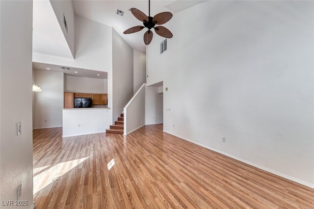 unfurnished living room featuring ceiling fan, light wood-type flooring, and a high ceiling