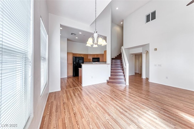 unfurnished living room featuring a high ceiling, an inviting chandelier, and light hardwood / wood-style floors