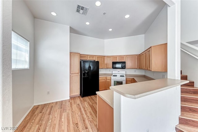 kitchen featuring a towering ceiling, light wood-type flooring, black appliances, and kitchen peninsula