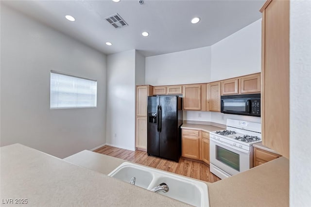 kitchen with light hardwood / wood-style flooring, sink, black appliances, a towering ceiling, and light brown cabinets