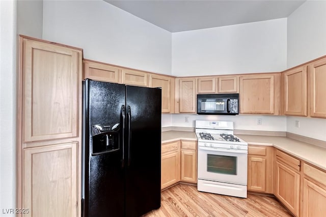 kitchen featuring a high ceiling, light brown cabinetry, black appliances, and light hardwood / wood-style flooring