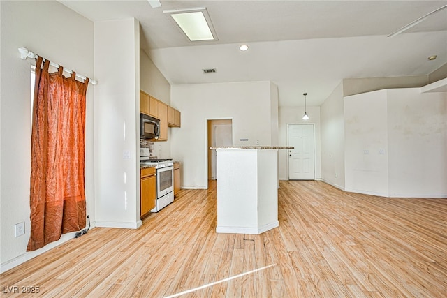 kitchen featuring light wood-type flooring, white gas stove, light brown cabinetry, and hanging light fixtures