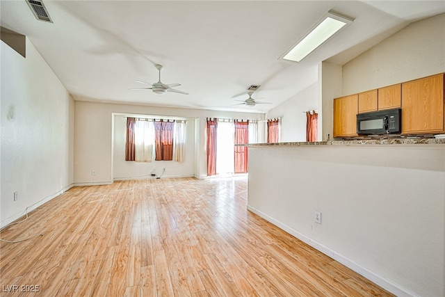 unfurnished living room featuring ceiling fan, vaulted ceiling with skylight, and light hardwood / wood-style flooring