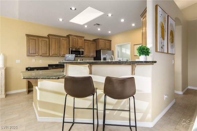 kitchen with dark stone countertops, a breakfast bar, kitchen peninsula, and appliances with stainless steel finishes