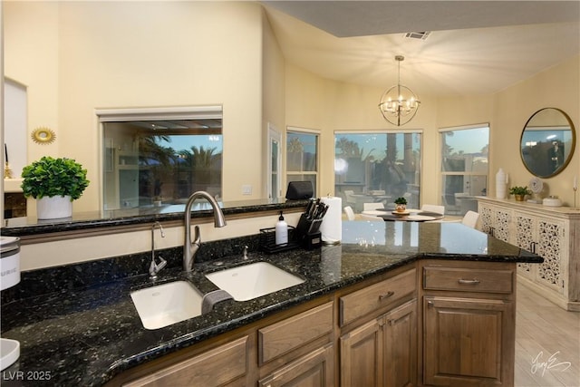 kitchen featuring sink, an inviting chandelier, dark stone countertops, and pendant lighting