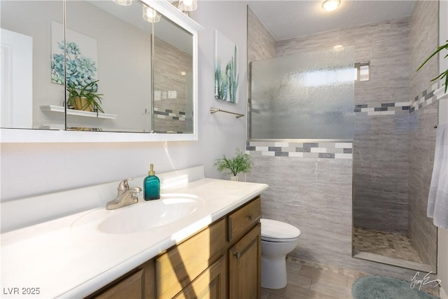 bathroom featuring tiled shower, vanity, and toilet