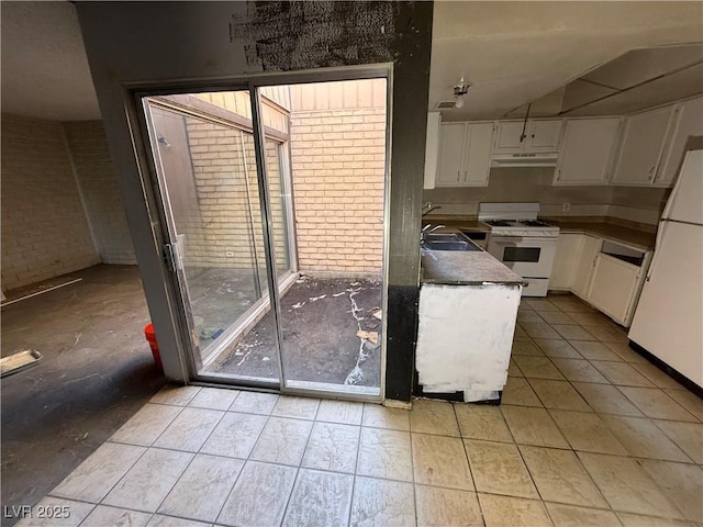 kitchen featuring white appliances, white cabinetry, a wealth of natural light, and brick wall