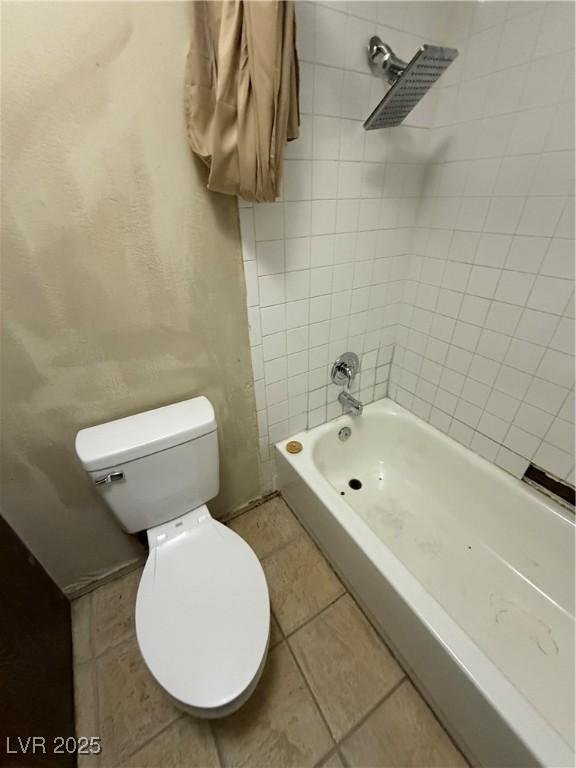 bathroom featuring tile patterned flooring, tiled shower / bath combo, and toilet