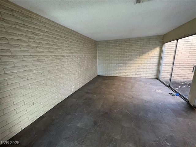 empty room featuring a textured ceiling and brick wall