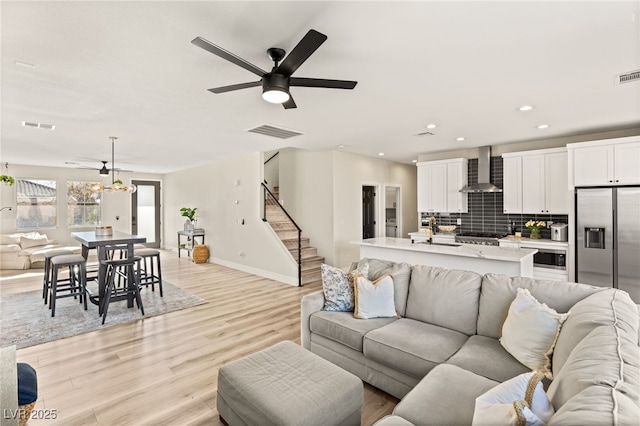 living room featuring ceiling fan with notable chandelier and light wood-type flooring