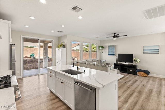 kitchen featuring stainless steel appliances, an island with sink, light stone counters, sink, and white cabinetry