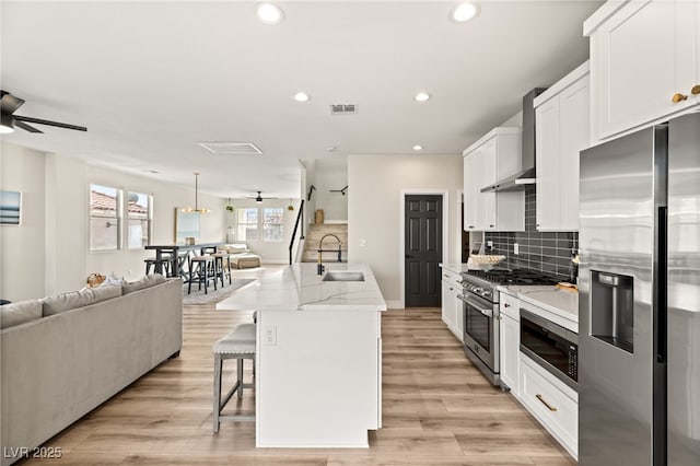 kitchen with wall chimney exhaust hood, a center island with sink, white cabinetry, appliances with stainless steel finishes, and sink