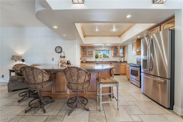 kitchen with a breakfast bar, a tray ceiling, dark stone counters, appliances with stainless steel finishes, and sink