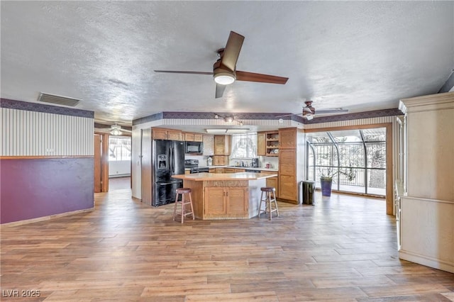 kitchen with a healthy amount of sunlight, black appliances, a kitchen breakfast bar, and a center island