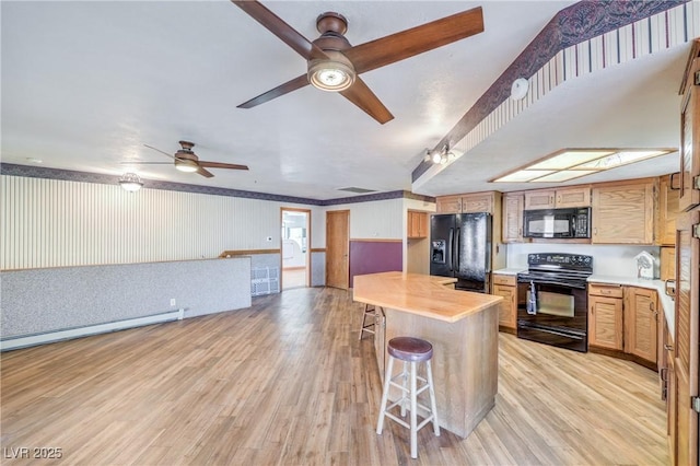 kitchen featuring a kitchen bar, ceiling fan, light hardwood / wood-style flooring, baseboard heating, and black appliances