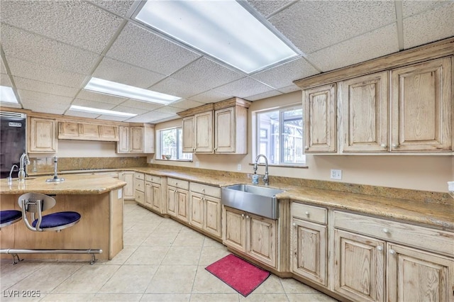 kitchen featuring light brown cabinetry, light tile patterned flooring, a paneled ceiling, and sink