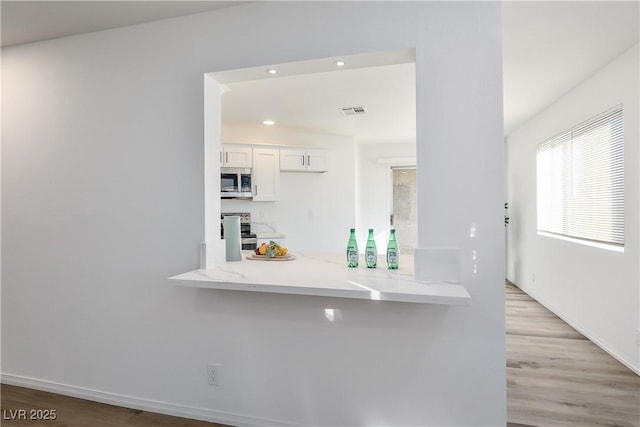 kitchen featuring light stone countertops, white cabinetry, light hardwood / wood-style floors, and appliances with stainless steel finishes