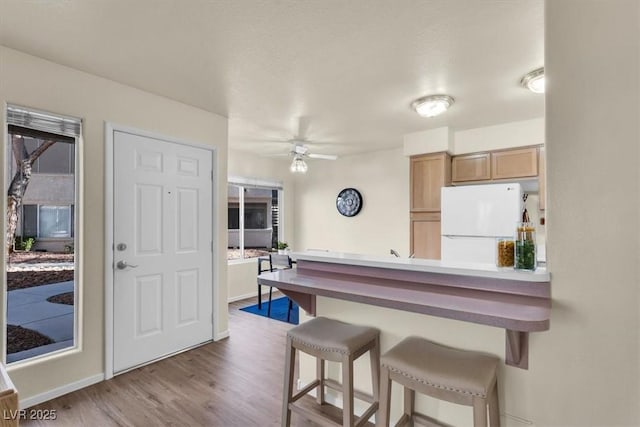 kitchen featuring white fridge, a kitchen breakfast bar, ceiling fan, wood-type flooring, and light brown cabinetry