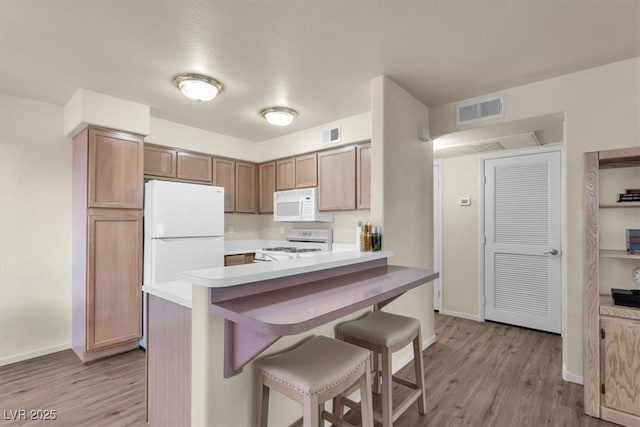 kitchen featuring white appliances, kitchen peninsula, light hardwood / wood-style floors, and a breakfast bar area