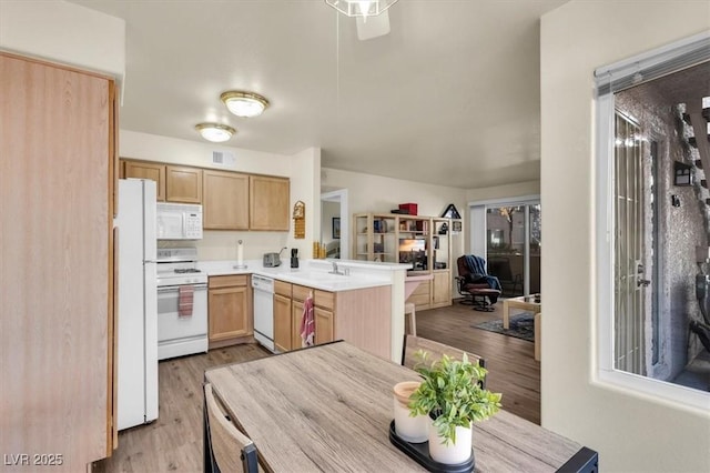 kitchen with white appliances, kitchen peninsula, light brown cabinetry, sink, and light hardwood / wood-style flooring