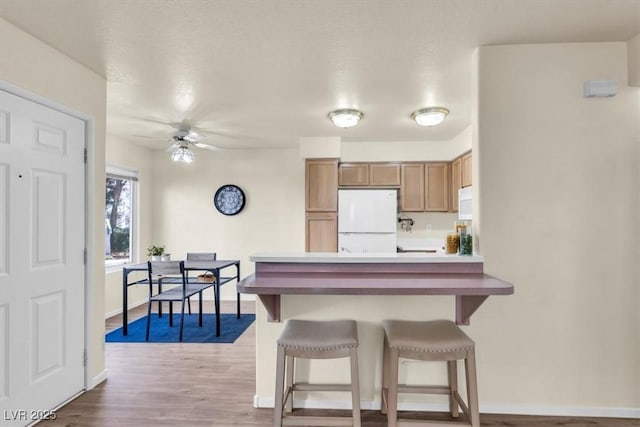 kitchen with light hardwood / wood-style floors, kitchen peninsula, ceiling fan, a breakfast bar, and white refrigerator